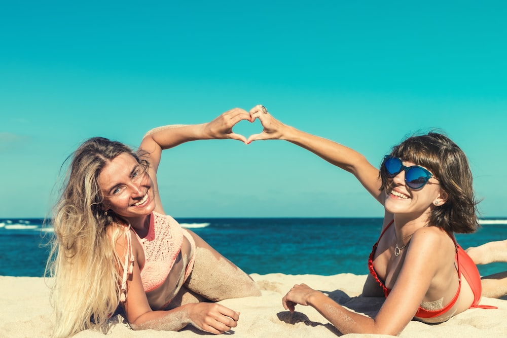 two women lying on seashore joining hands forming heart