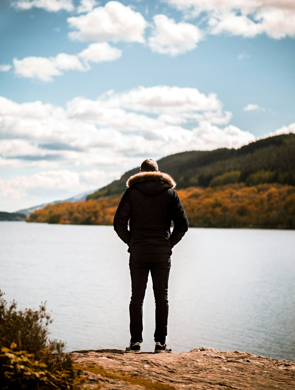 pessoa vestindo jaqueta em pé na frente de um corpo de água calmo durante o dia