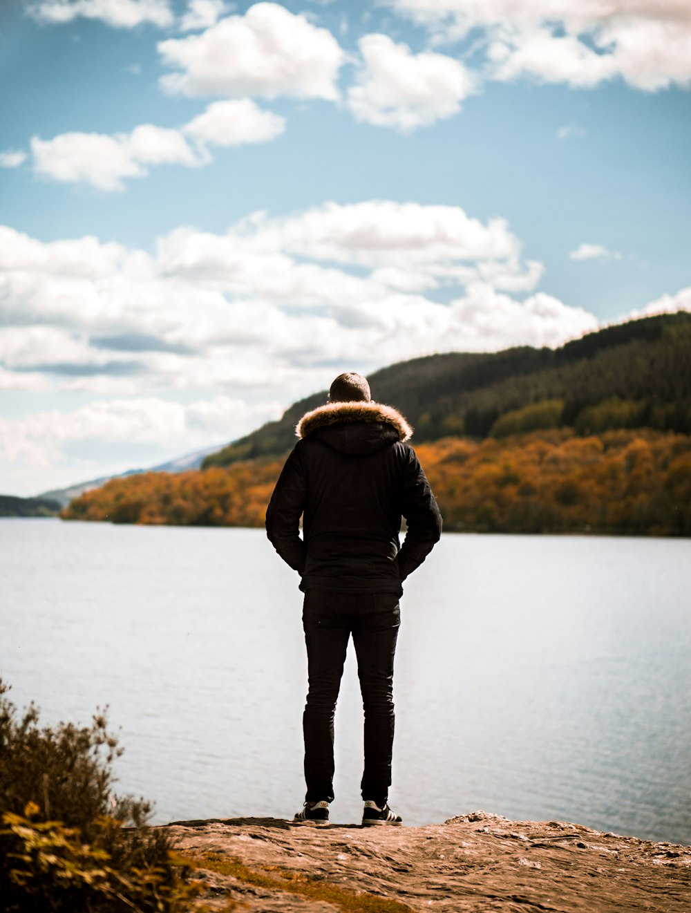 person wearing jacket standing on front of calm body of water during daytime