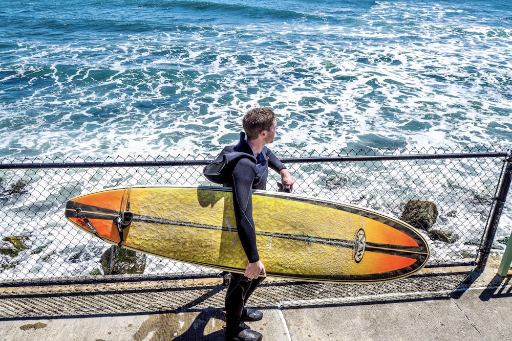 man holding yellow and black surfboard near sea during daytime