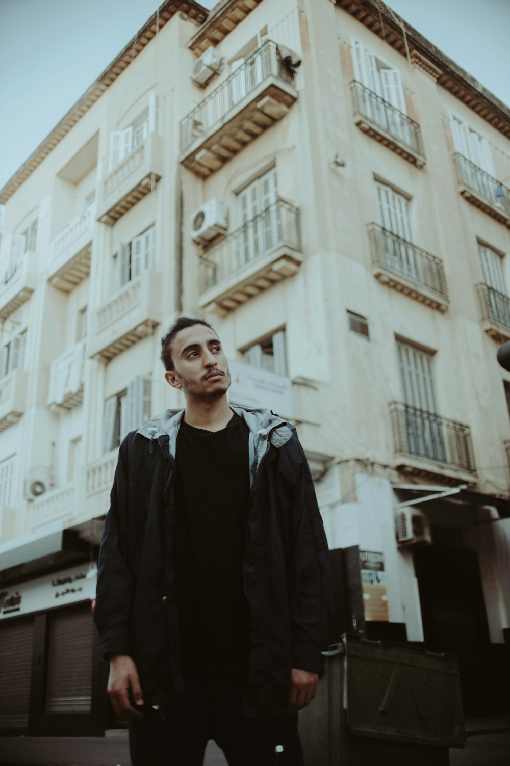 man in black hoodie in front of beige building