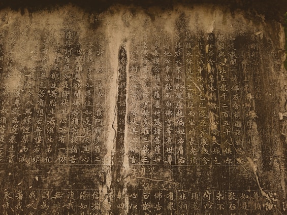 Vertical columns of ancient script cover a weathered stone surface, with faded and unevenly colored sections suggesting age and wear.