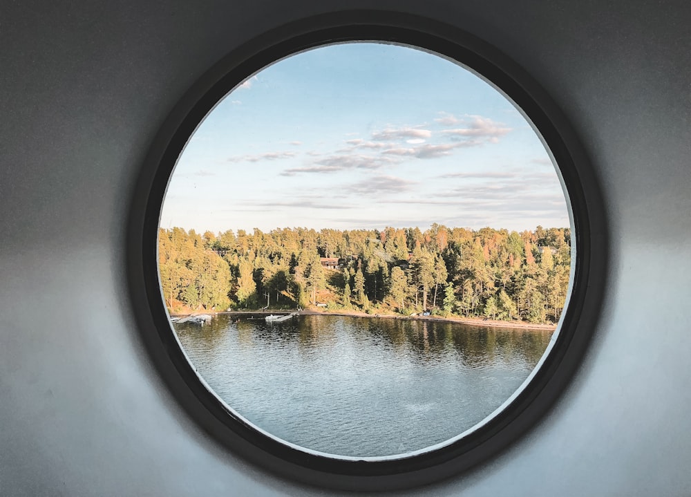 Grüne Bäume am Ufer durch rundes Fenster gesehen