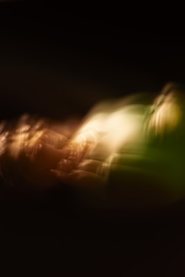 Blurred and abstract image with flowing light patterns creating a sense of motion. Warm earth tones mixed with green hues dominate the scene, providing an ethereal and dreamlike quality.