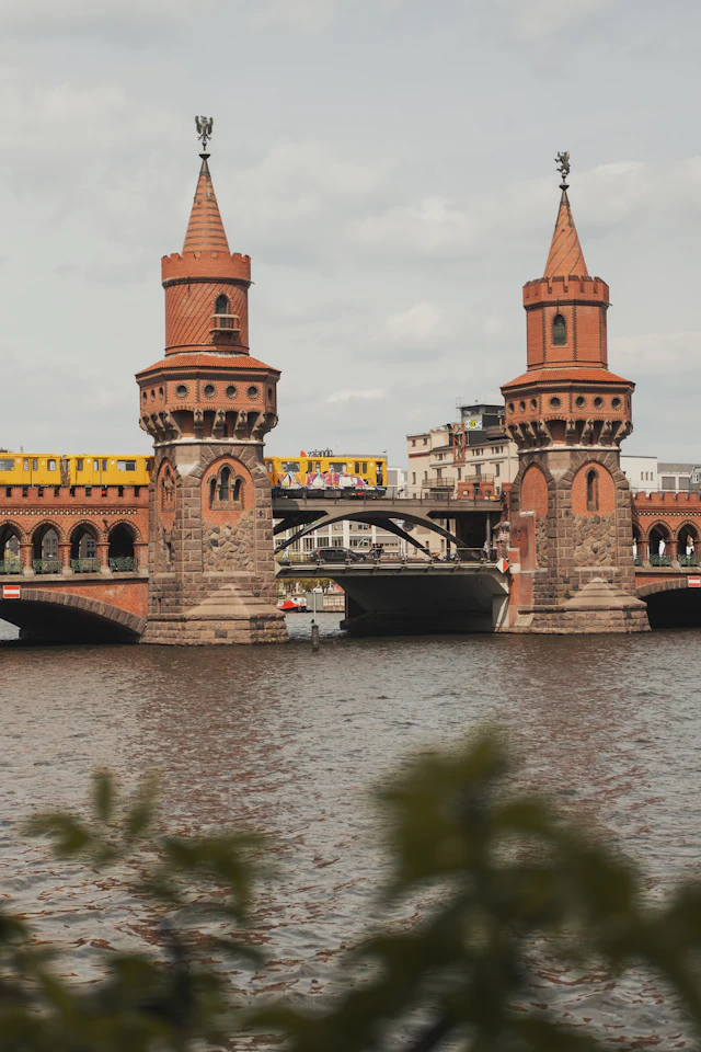 The twin red-brick towers of the Oberbaum Bridge span the Spree River between Kreuzberg and Friedrichshain, with a yellow U-Bahn train crossing.