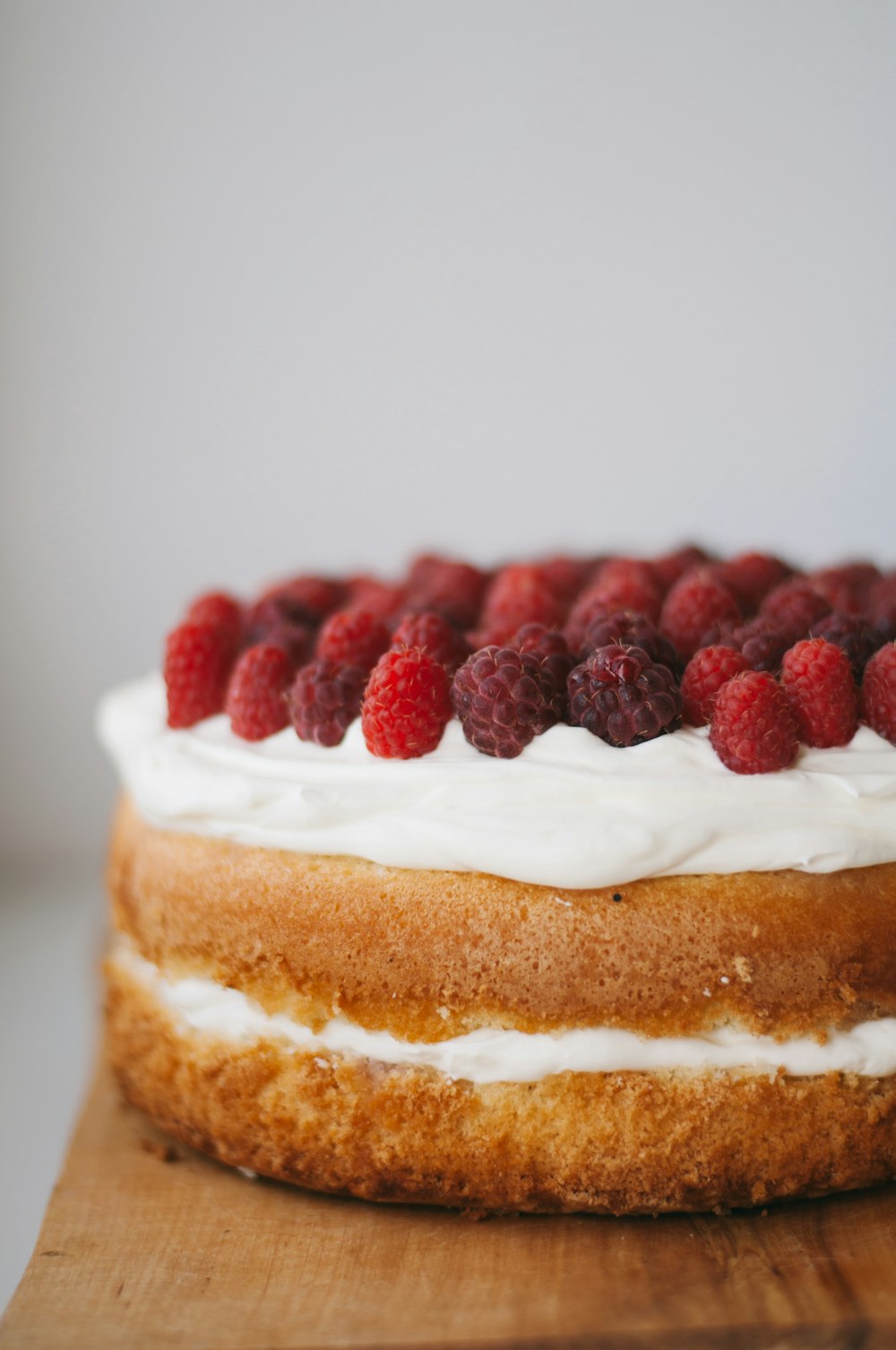 赤いラズベリーをトッピングした白いフロスティングの丸いケーキ
