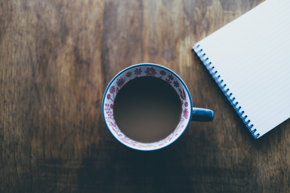 chocolate drink in mug near blue spiral notebook