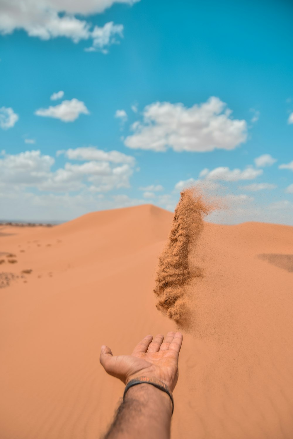 persona che getta sabbia sulla duna di sabbia del deserto
