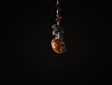 A small decorative object featuring a spiral seashell, intricately paired with black and white patterned beads. The object is suspended against a stark black background, creating a dramatic contrast that emphasizes the details of the seashell and beads.