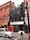 A street scene featuring a multi-story brick building with red window frames, a black-tiled building with a white sign that reads 'white space,' and a classic red telephone booth. A grey taxi is driving past, and there is a traffic light pole in the foreground.