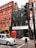 A street scene featuring a multi-story brick building with red window frames, a black-tiled building with a white sign that reads 'white space,' and a classic red telephone booth. A grey taxi is driving past, and there is a traffic light pole in the foreground.
