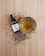 A small glass bowl filled with yellow-green oil is placed on a wooden surface, surrounded by scattered hemp seeds. Next to the bowl is a dropper bottle labeled as CBD oil.