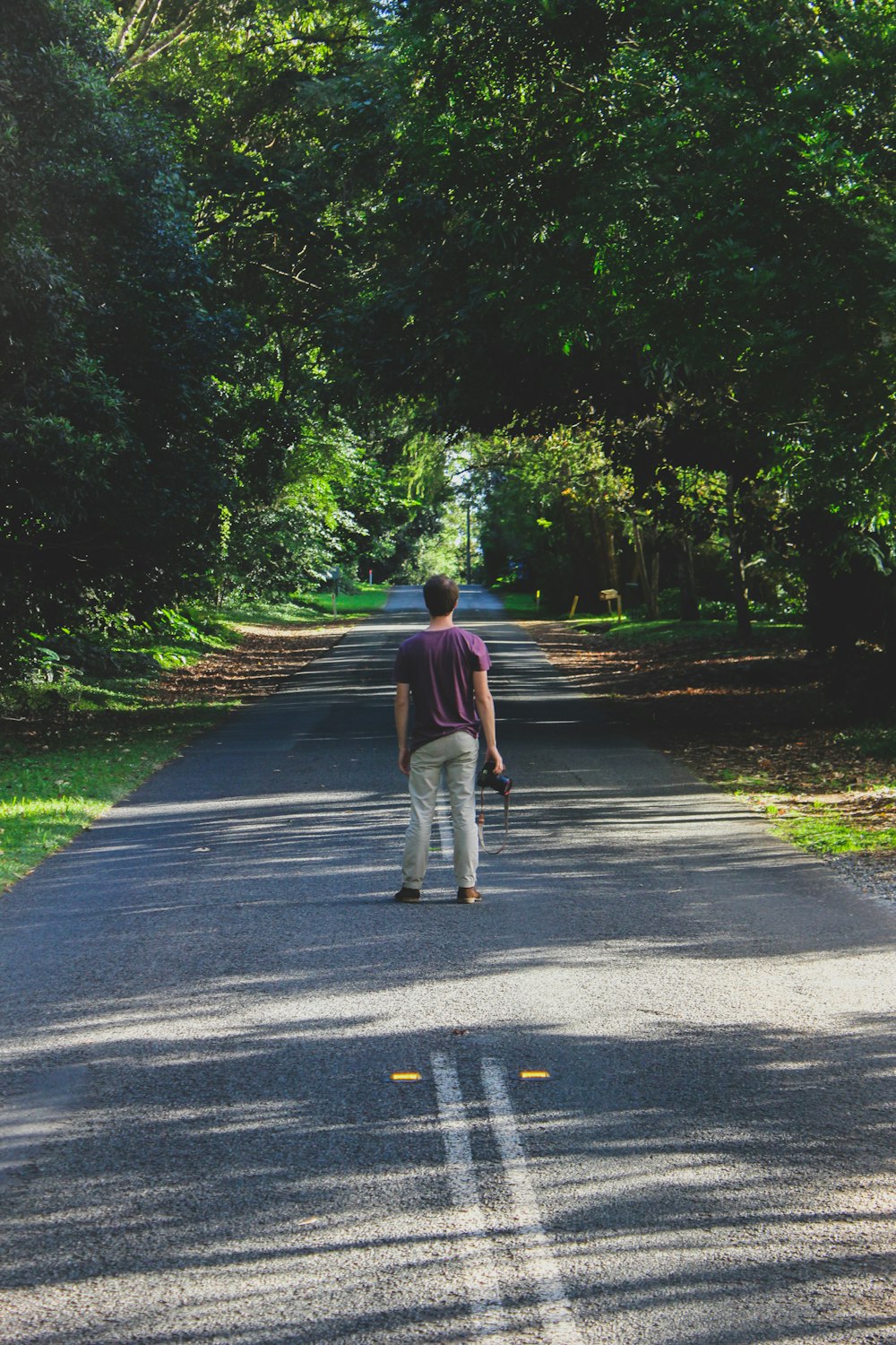 man standing on road between trees during daytime