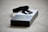 A black electronic device, possibly a fitness tracker or smartwatch, is resting on top of its packaging. The box is predominantly black and white with a large number three printed on it, suggesting a model or version number. The surface underneath is a beige carpet.
