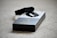 A black electronic device, possibly a fitness tracker or smartwatch, is resting on top of its packaging. The box is predominantly black and white with a large number three printed on it, suggesting a model or version number. The surface underneath is a beige carpet.