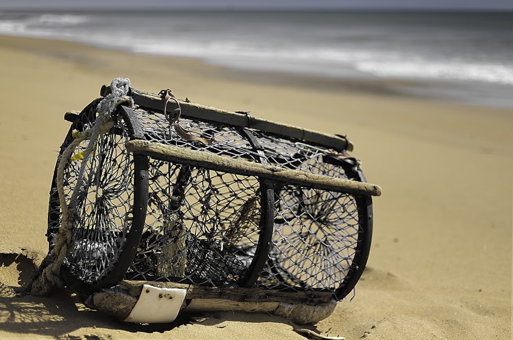 selective focus photography of cylindrical black cage on seashore