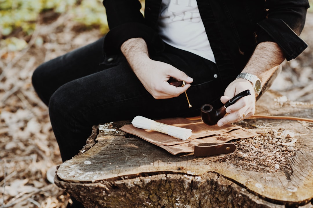 man holding tobacco while sitting on wood slab