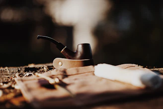 A close-up of a beautifully crafted smoking pipe made from natural wood, resting on a bed of green leaves.