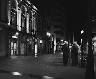 Black and white photograph of elderly neighbors gathered around a street corner in El Pedregal, sharing memories.