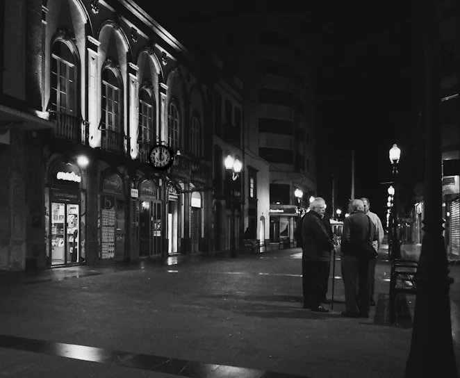 Black and white photograph of elderly neighbors gathered around a street corner in El Pedregal, sharing memories.
