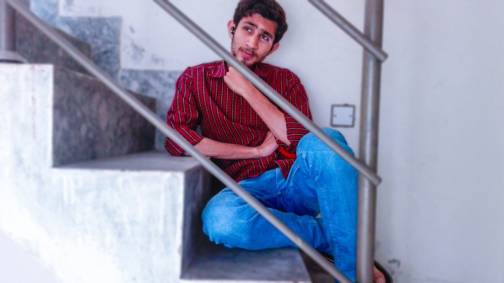 man in red shirt and blue jeans sitting on stair