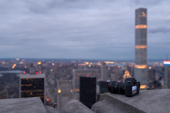 A sleek film camera lens capturing a dramatic cityscape at dusk with deep shadows and vibrant highlights.