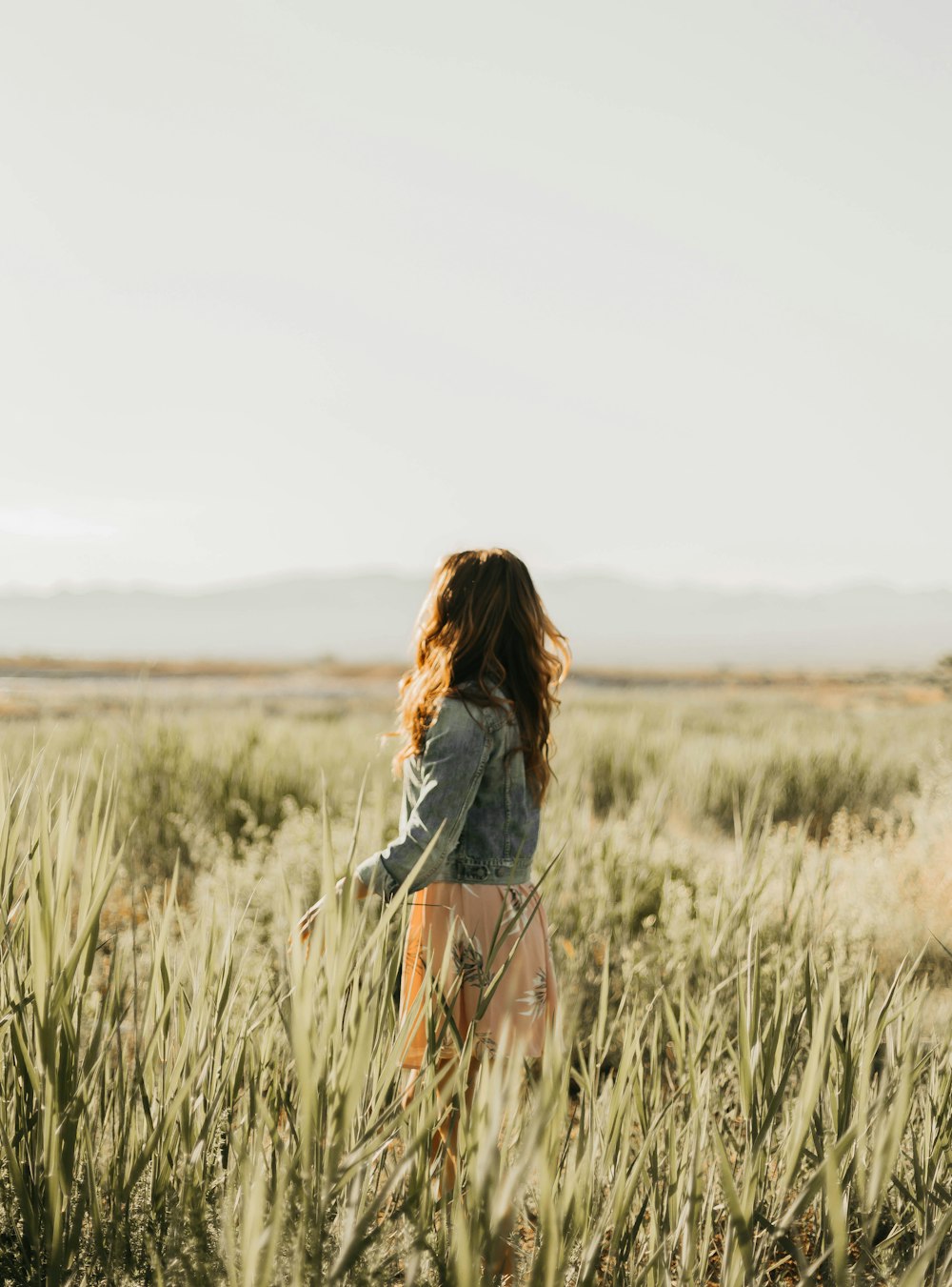 woman in gray denim jacket standing in tall grass field during daytime