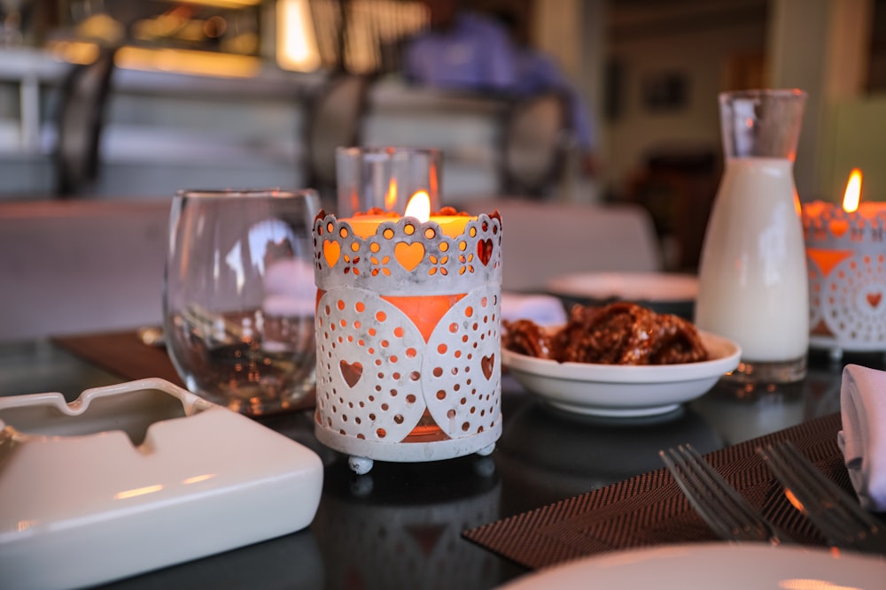 candle in container beside table and drinking glass