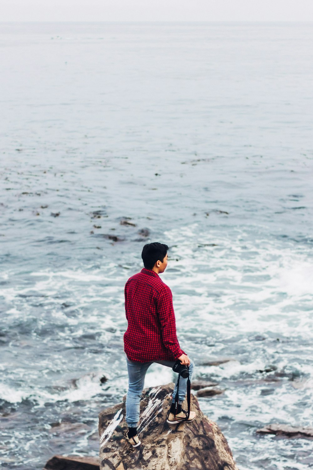 man wearing red dress shirt standing on seashore rock during daytime