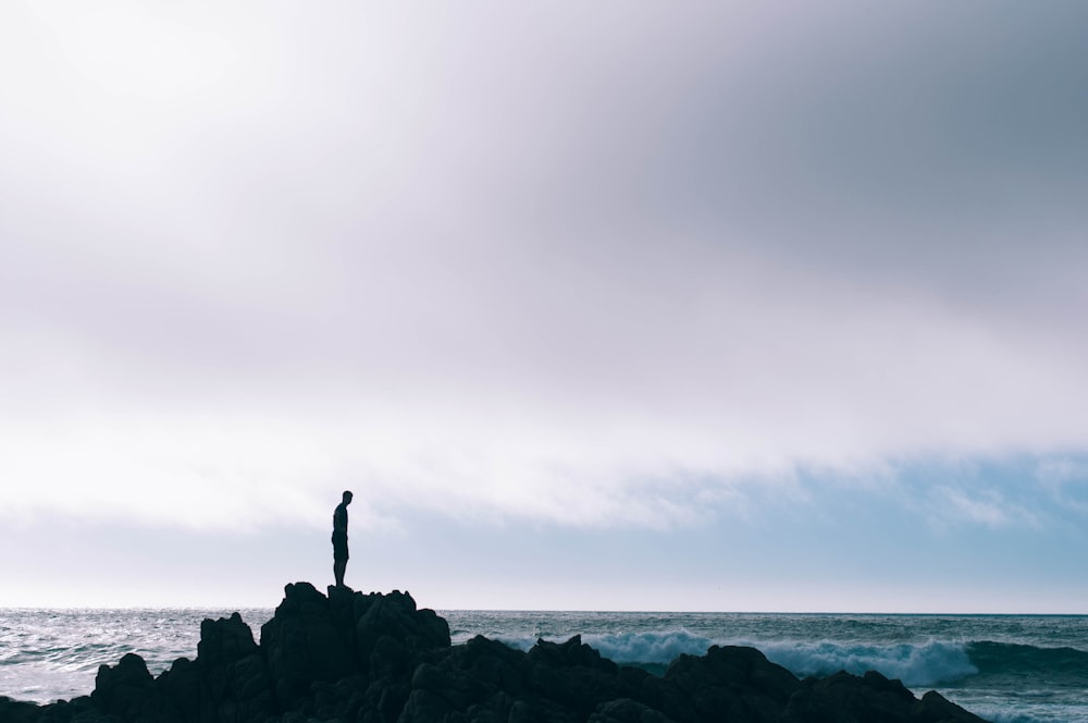man standing on boulder in front of ocean