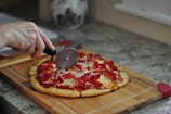 A person slicing a homemade pizza with a golden crust in a cozy kitchen.