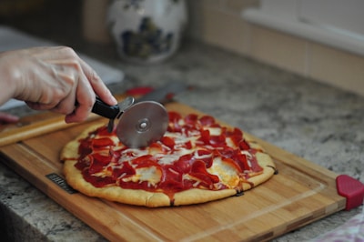 A person slicing a homemade pizza with a golden crust in a cozy kitchen.