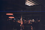 Warm moment inside a local food market with customers browsing colorful stalls under pendant lighting.