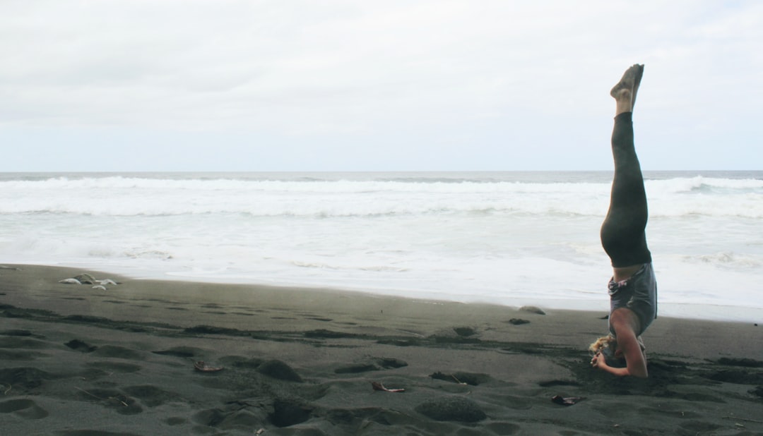 woman doing yoga exercise by inverting her body near seashore