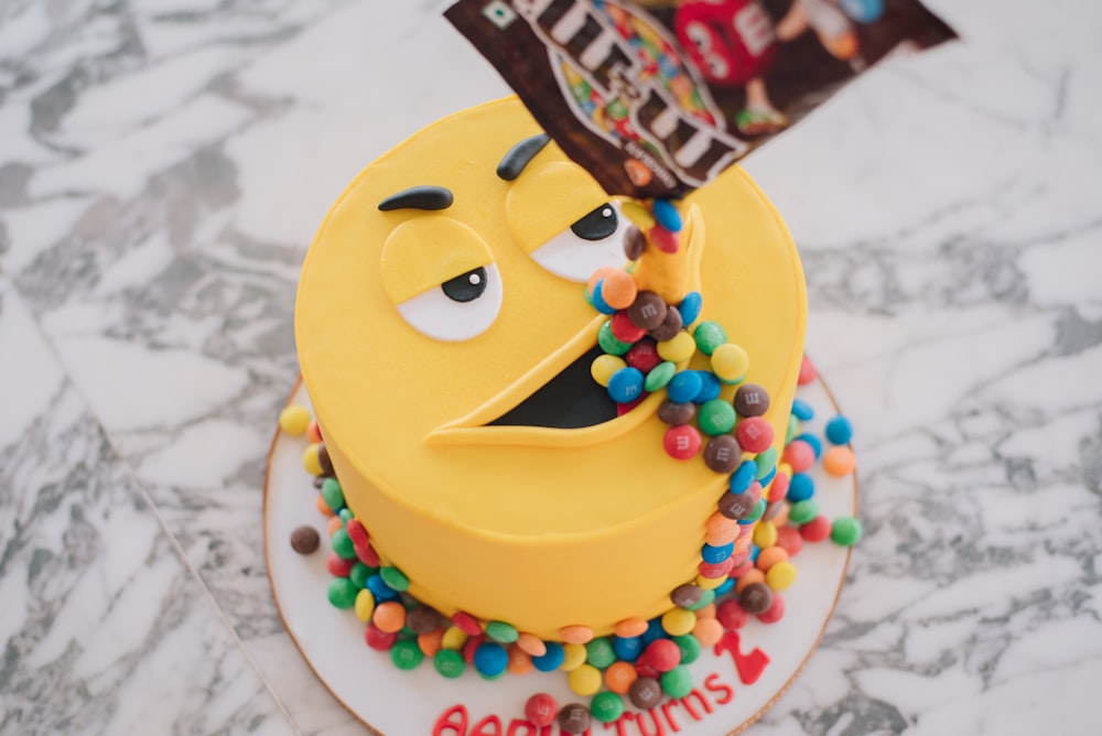 M&M pack pouring candies on M&m cake's mouth on marble surface