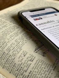 silver iPhone X displaying cannabis definition on top of dictionary