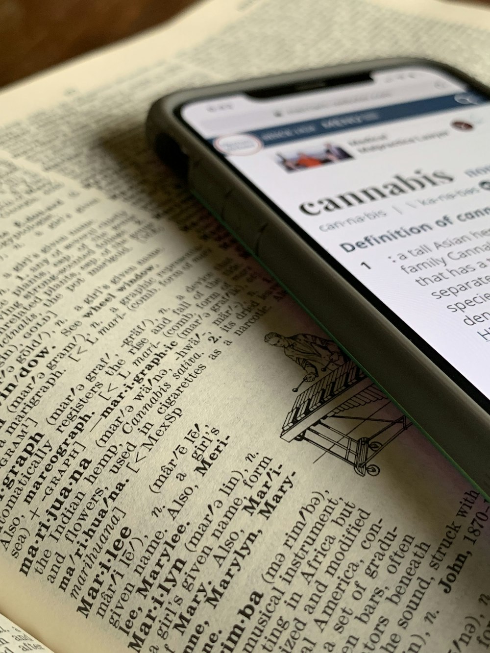 silver iPhone X displaying cannabis definition on top of dictionary