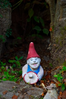 Colorful ceramic garden gnome standing cheerfully beside lush green plants