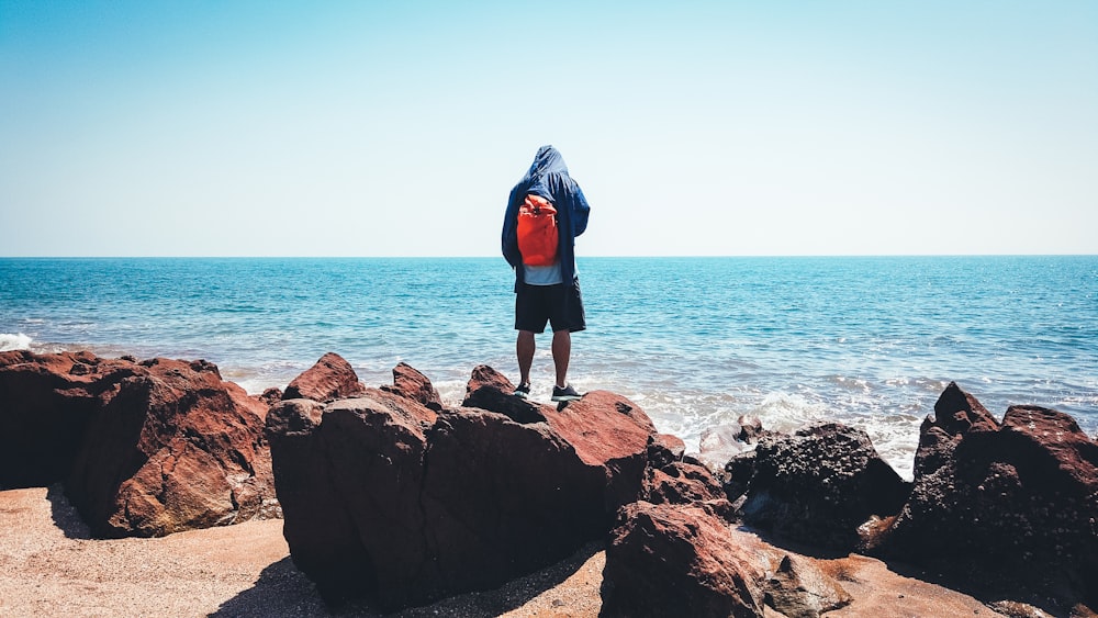 pessoa em pé na rocha marrom vendo o mar azul sob o céu azul e branco