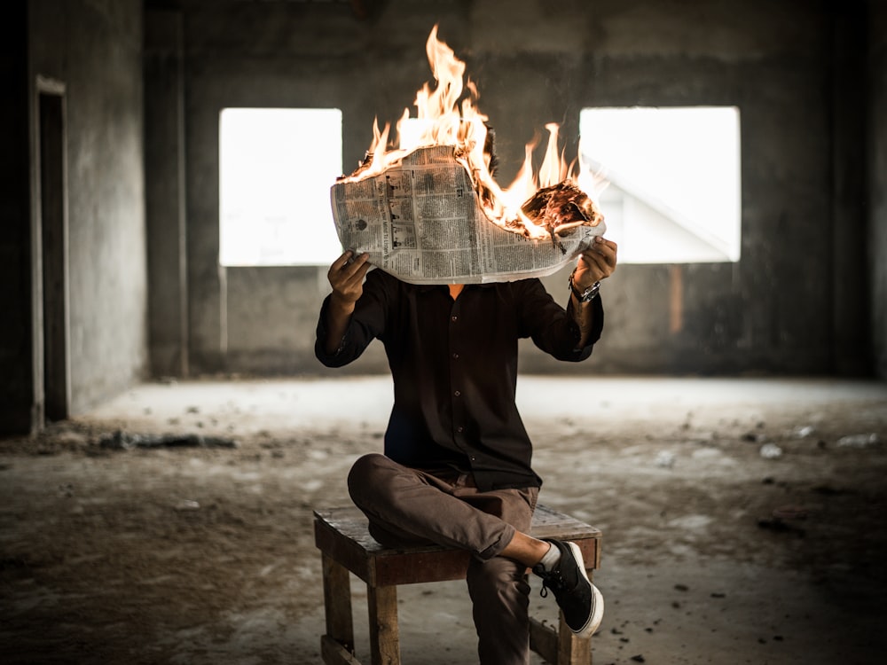 hombre sentado en una silla sosteniendo un periódico en llamas