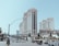 A bustling street scene with heavy traffic and prominent buildings. The architecture features a grand style, with tall, ornate structures like Caesars Palace. Vehicles of various types are seen on the road, and a green street sign indicates Las Vegas Boulevard. There is a clear sky in the background.