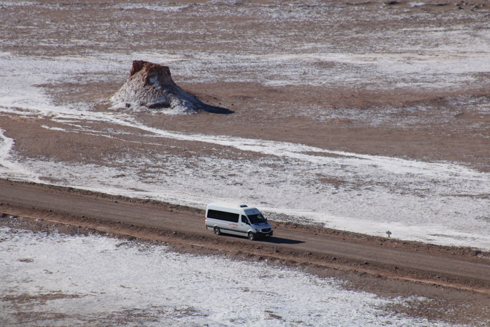 white passenger van travelling on road across desert