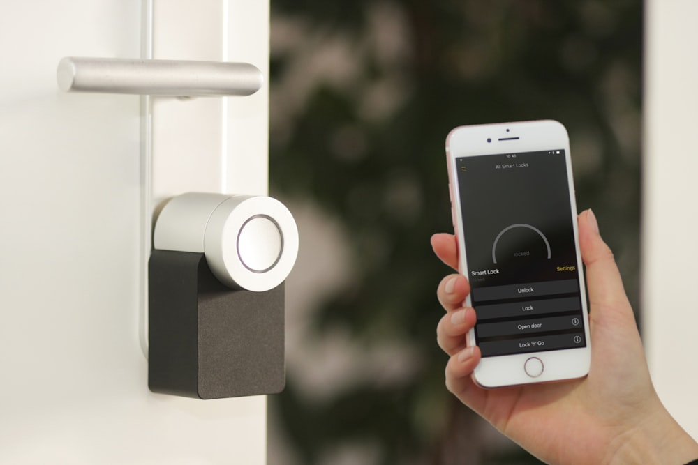 Person holding white mobile phone and using an app to control the locks on the door to their home.