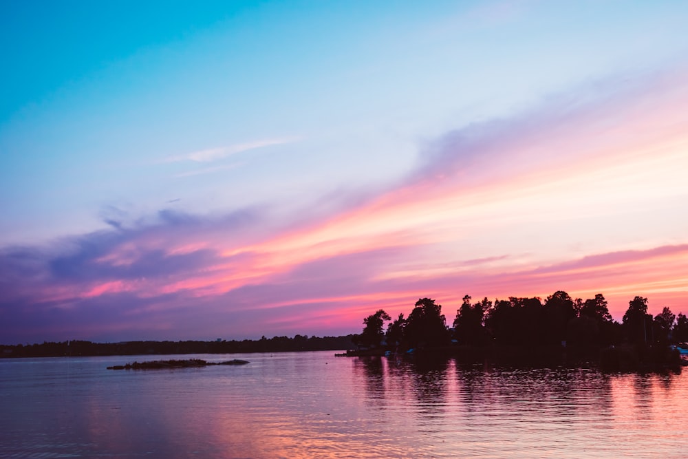 body of water near trees at golden hour