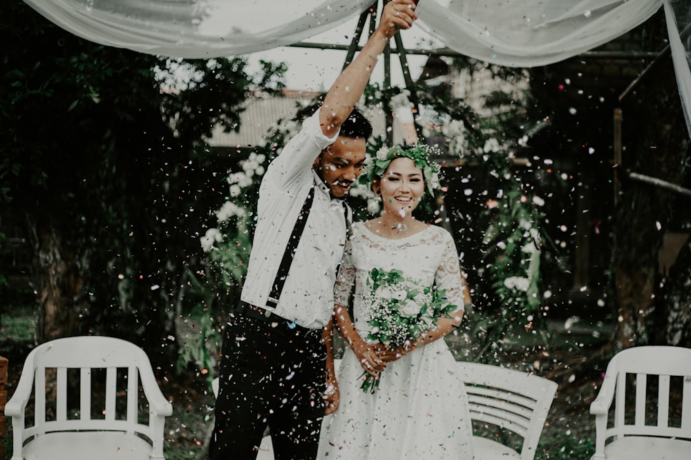 man raising his right arm beside woman holding bouquet of flowers