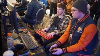 man using video game control pad beside man using computer keyboard sitting and playing video games