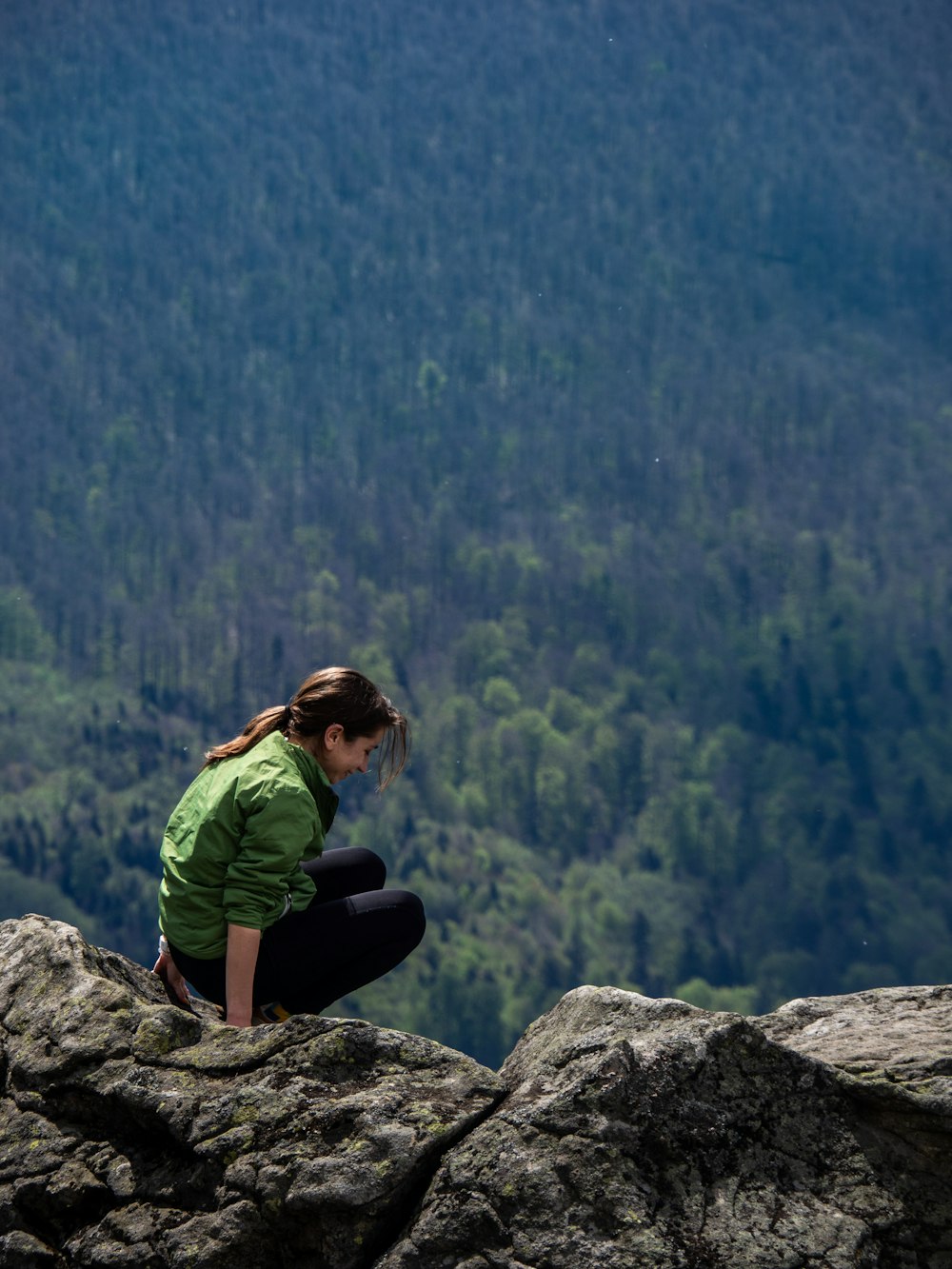 woman sitting on rocky mountain near the forest