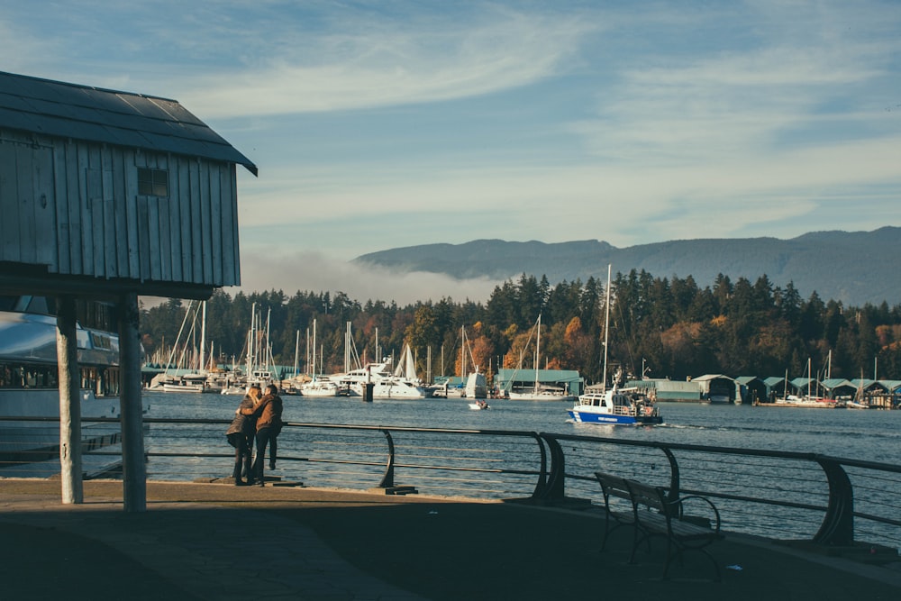 two men leaning on metal railing overlooking boats in the sea