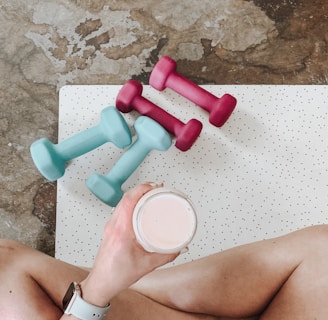 person holding white liquid filled cup above two pairs of dumbbells