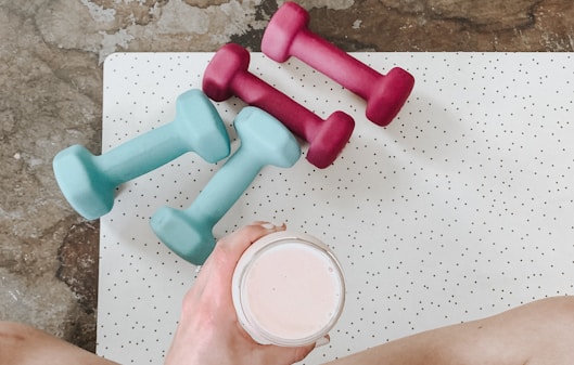 person holding white liquid filled cup above two pairs of dumbbells